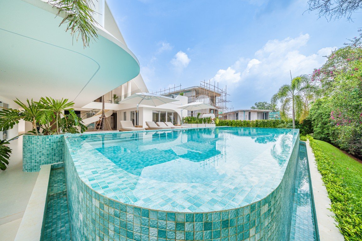 Luxurious resort pool with turquoise tiled edge, white modern building and lounge chairs under umbrellas in bright sunshine.