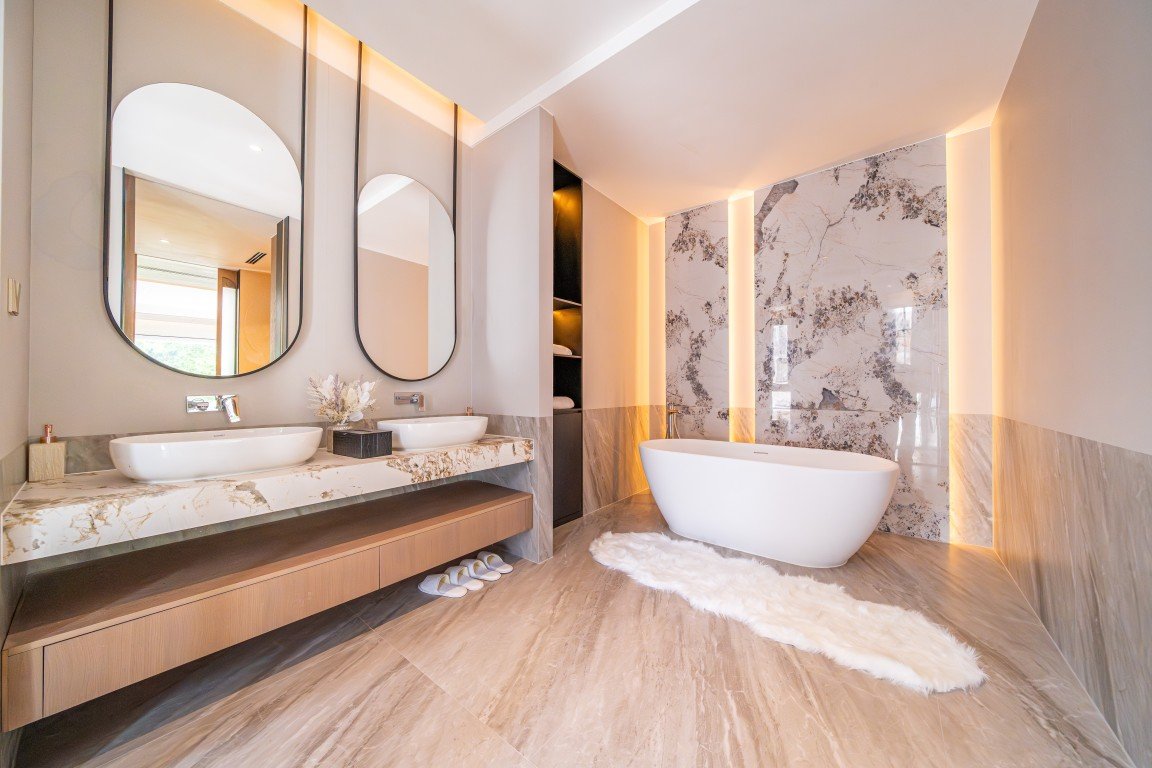 Luxurious bathroom with double vessel sinks, marble countertop, and large oval mirrors.