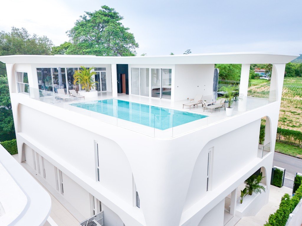 White modern villa rooftop terrace with a rectangular pool, glass railing, lounge chairs, and potted plants