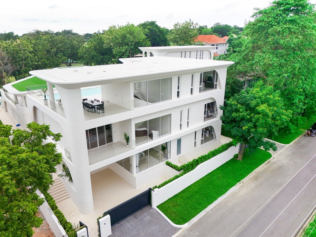 Modern white multi-story residential building with curved balconies and large glass windows, set along a tree-lined street.