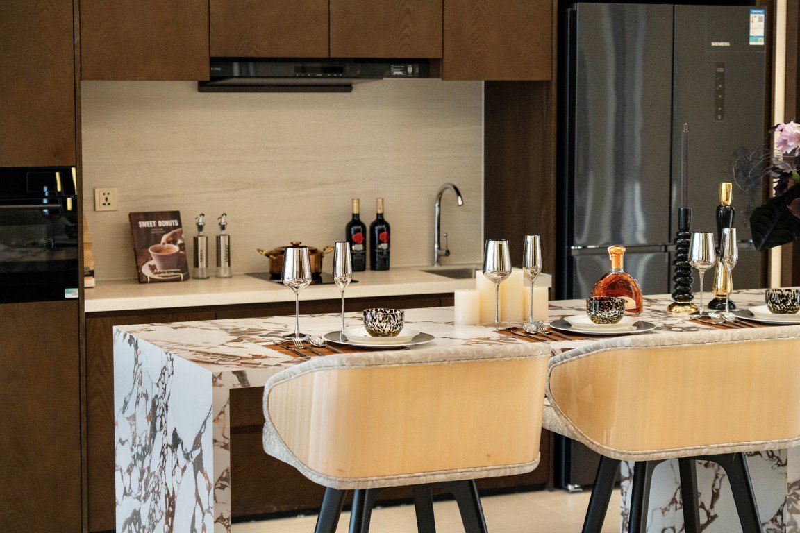 Marble kitchen island set for a dinner with candles, wine, and champagne flutes; brown bar stools nearby.
