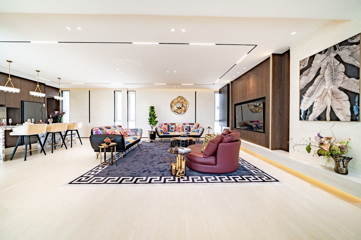 Open-concept living room with colorful sofas, a dark area rug with a Greek-key border, and a wall fireplace.
