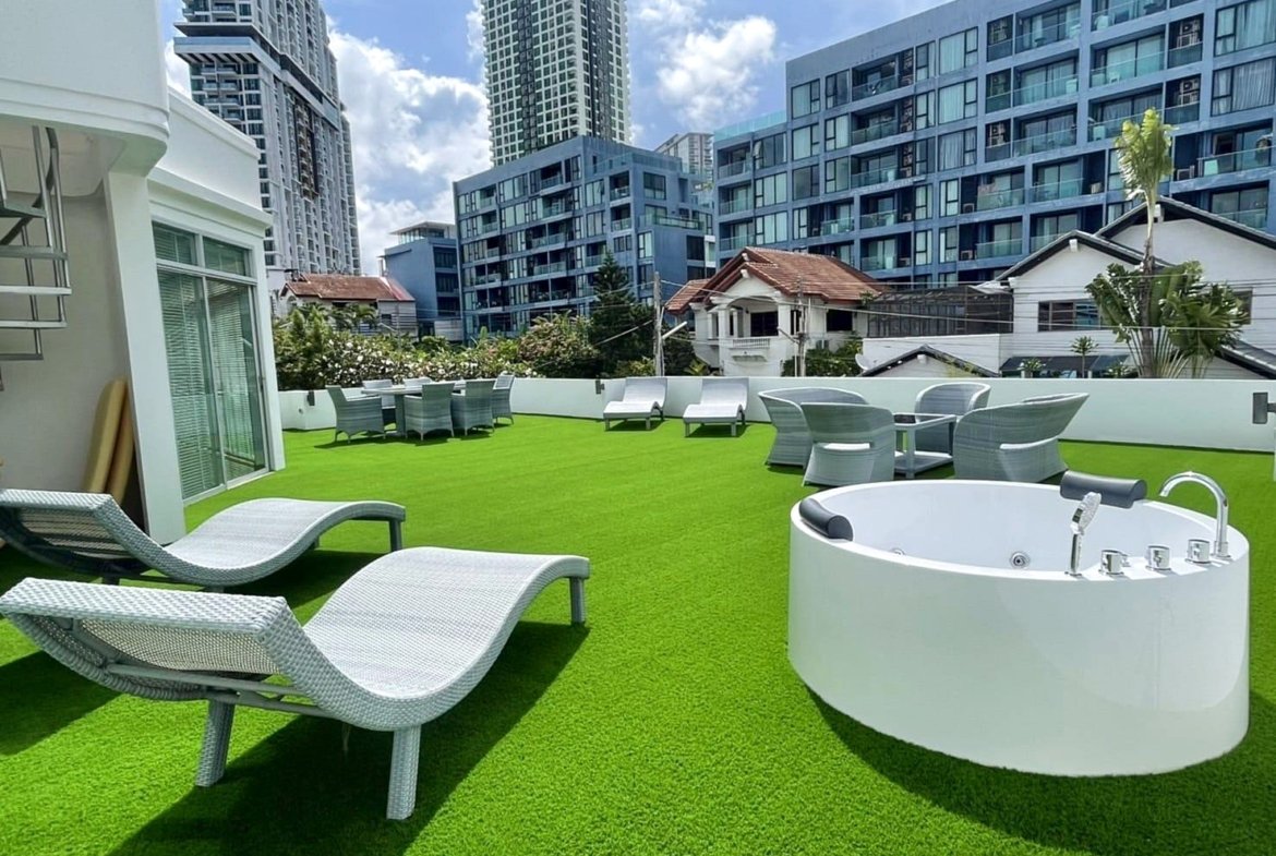 Rooftop terrace with bright green artificial grass, white lounge chairs, and a circular white hot tub, city buildings in the background
