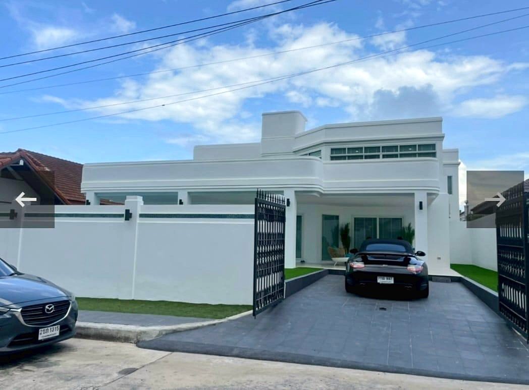 Modern white two-story house with an open wrought-iron gate; black sports car parked in the driveway, gray car at the curb on the left.