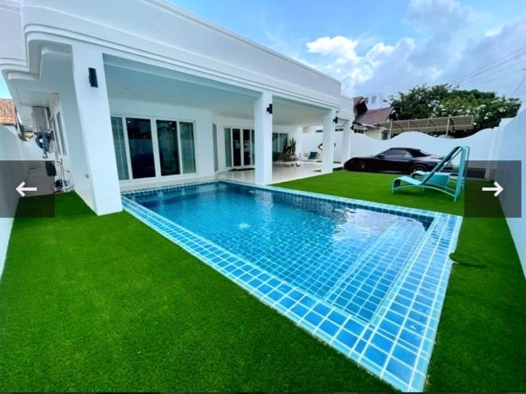 Backyard with a rectangular blue tiled pool white house and green artificial grass a black car sits on the driveway in the background