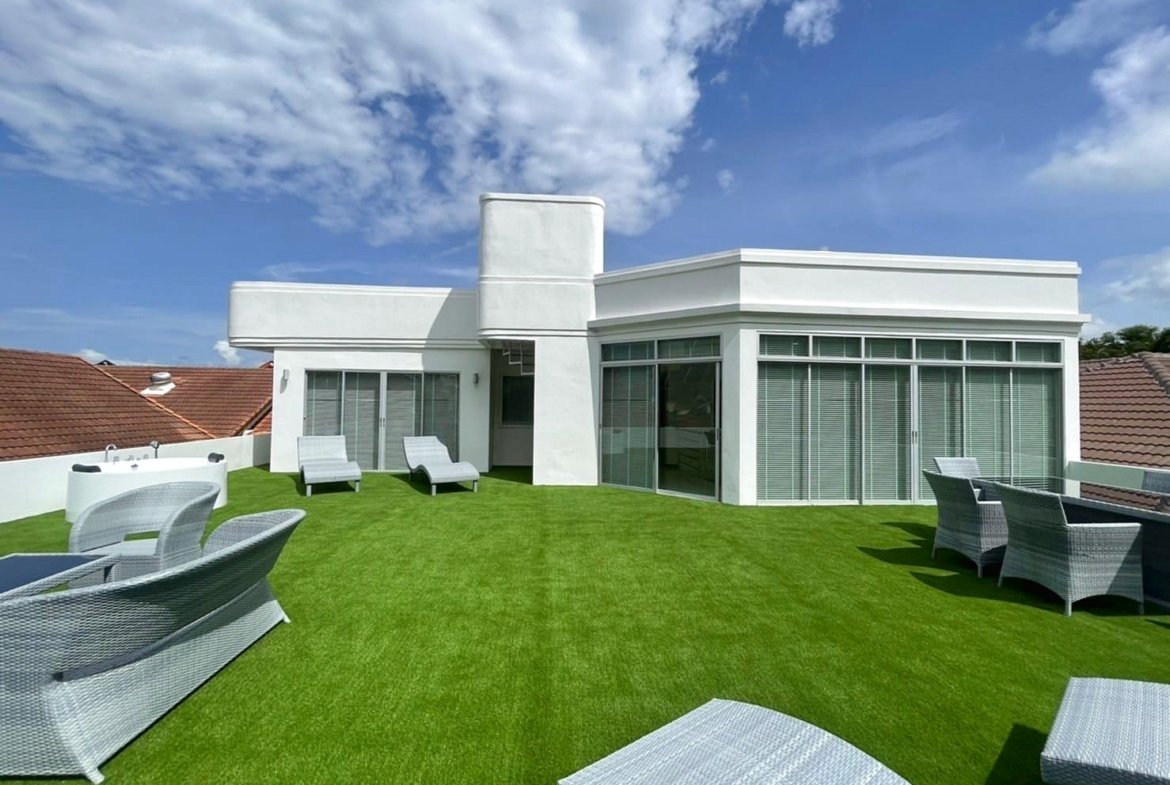 White modern rooftop terrace with decorative white furniture on bright green artificial grass under a blue sky.