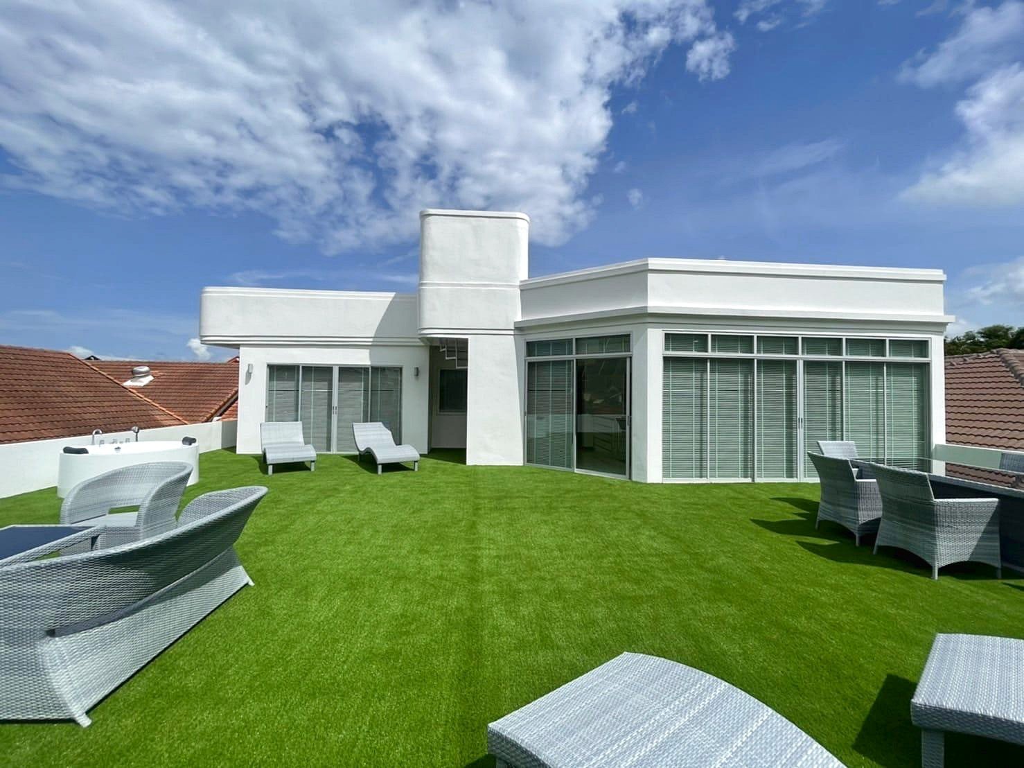 Casa_Jomtien_Village_Rent_Rdl346_9 White modern rooftop terrace with decorative white furniture on bright green artificial grass under a blue sky.