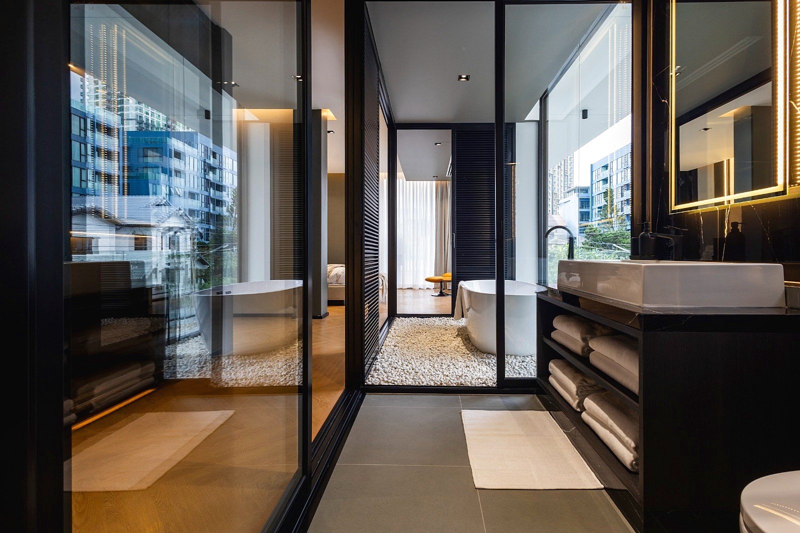 Casa_Jomtien_Village_Rent_Rdl352_14 Luxurious modern bathroom with glass walls, pebble floor, freestanding tub, and backlit mirror.
