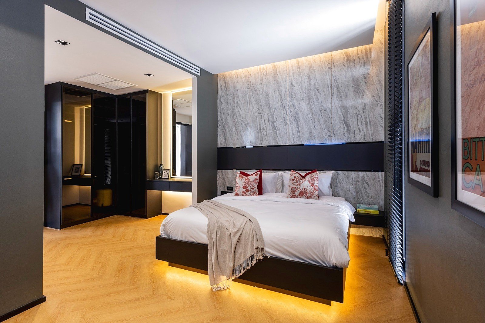 Casa_Jomtien_Village_Rent_Rdl352_16 Modern hotel bedroom with white bed, grey marble accent wall, red-patterned throw pillows, and warm under-bed lighting.