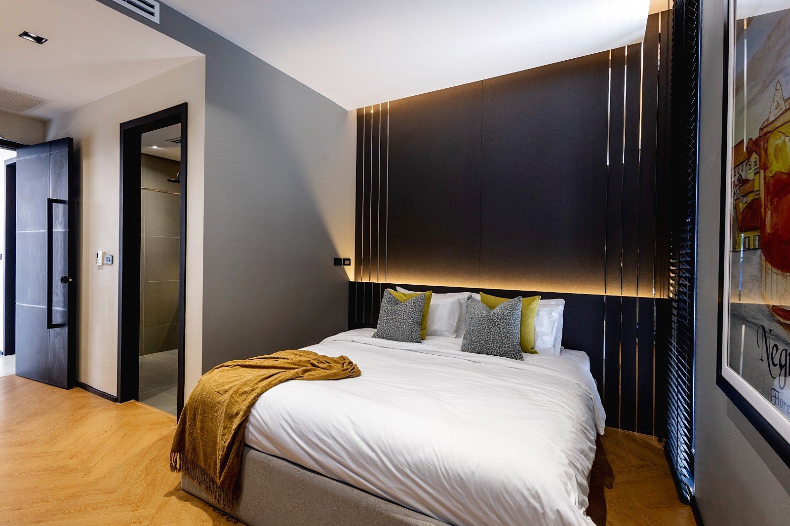 Casa_Jomtien_Village_Rent_Rdl352_20 Modern hotel bedroom with a king bed, white linens, mustard throw, and a dark paneled headboard with warm backlighting.