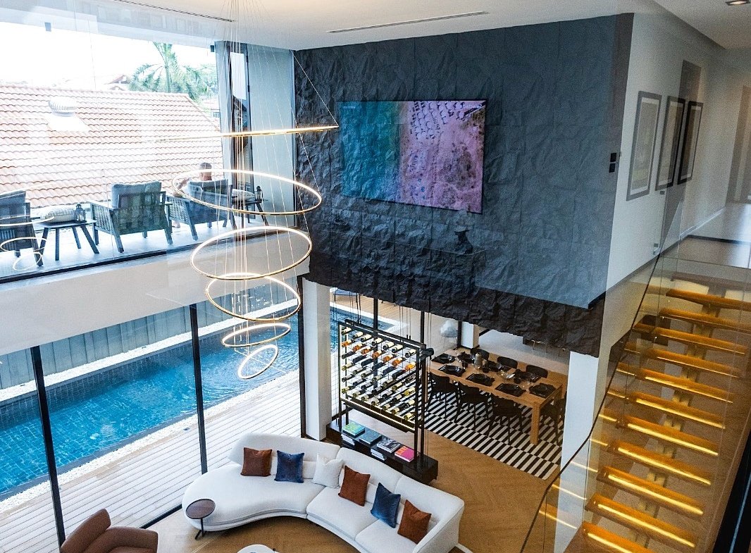 Two-story modern living room with a white curved sofa, colorful cushions, and circular pendant chandelier overlooking a pool terrace.