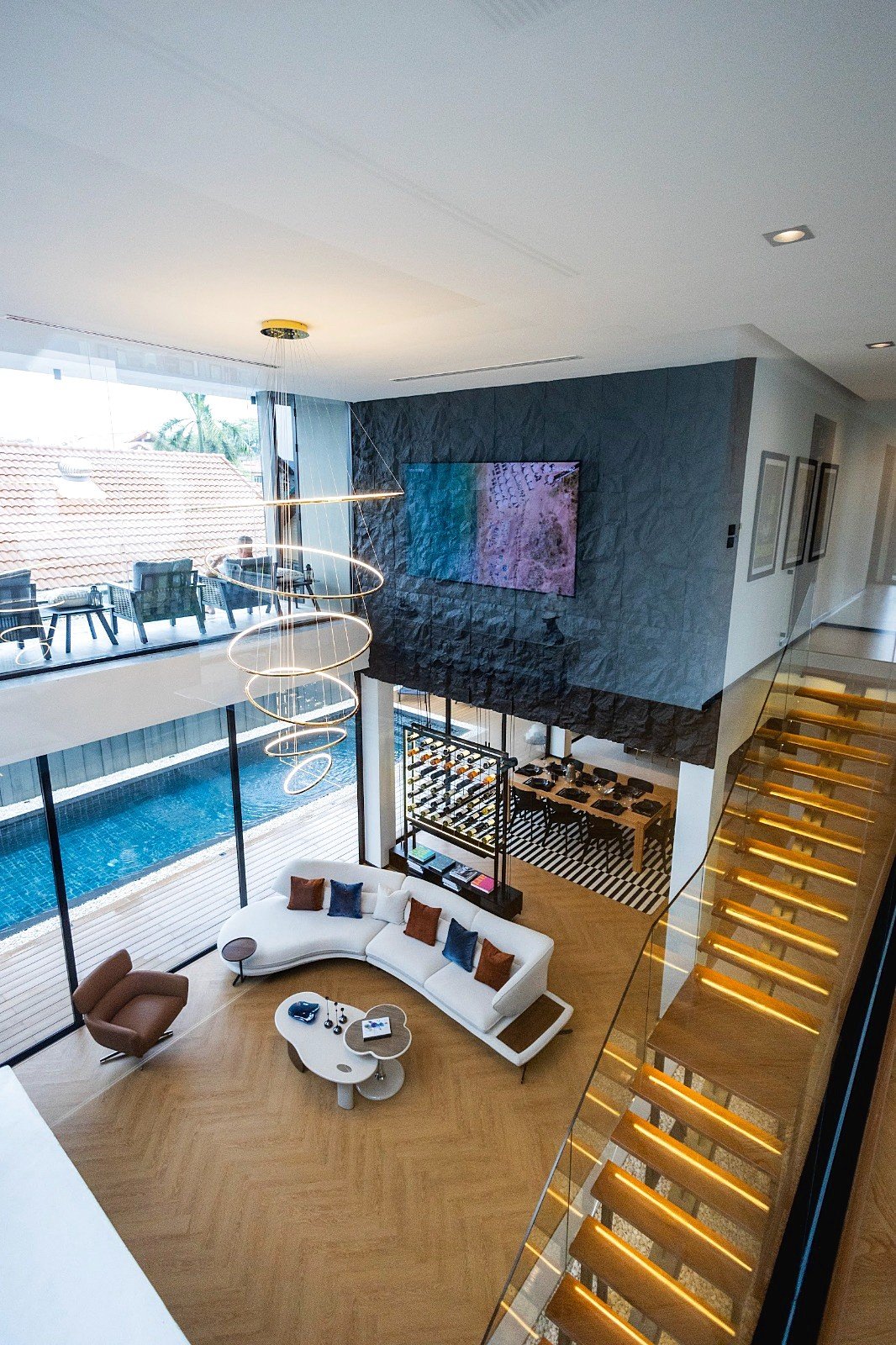 Casa_Jomtien_Village_Rent_Rdl352_24 Two-story modern living room with a white curved sofa, colorful cushions, and circular pendant chandelier overlooking a pool terrace.
