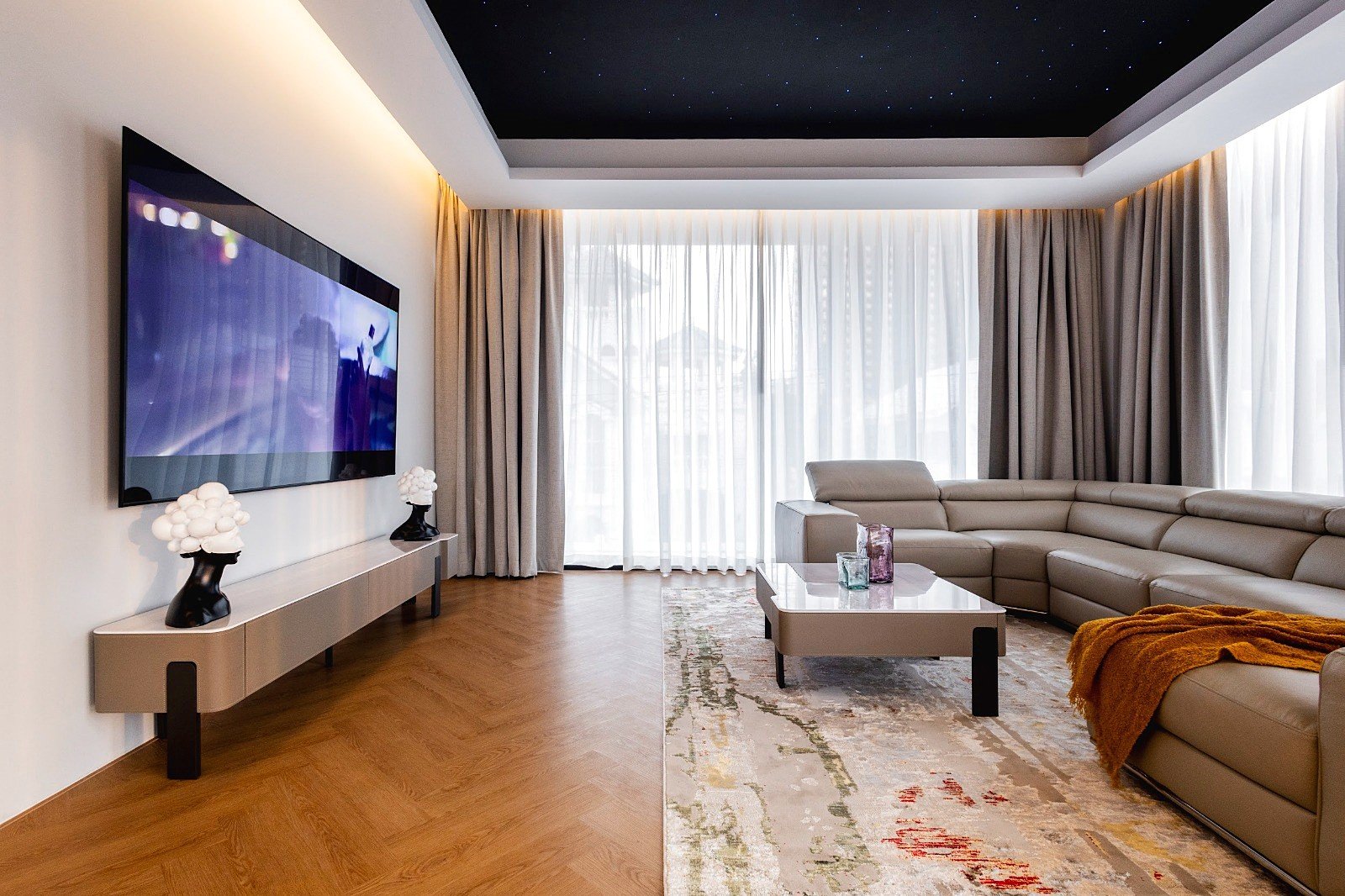 Casa_Jomtien_Village_Rent_Rdl352_37 Modern living room with a wall-mounted TV, beige sectional sofa, and glass-top coffee table under a starry ceiling.