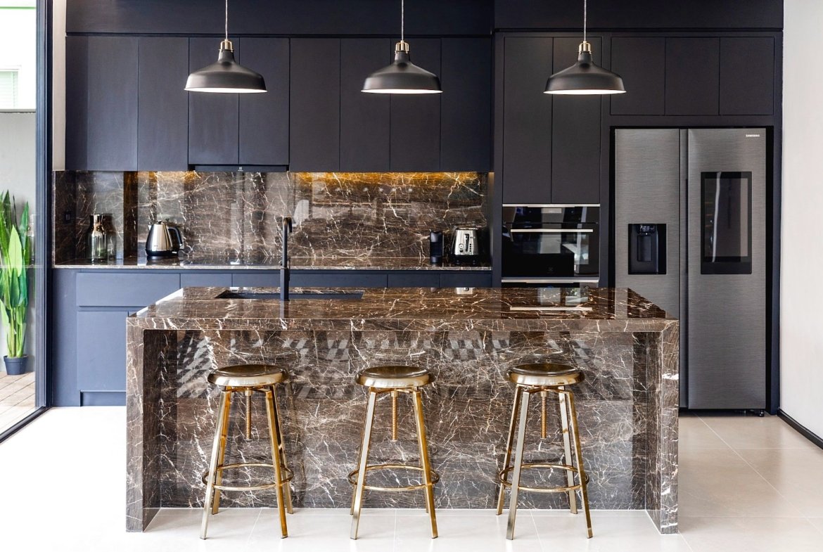 Modern black kitchen with a marble island and matching backsplash, three gold bar stools, and stainless appliances.