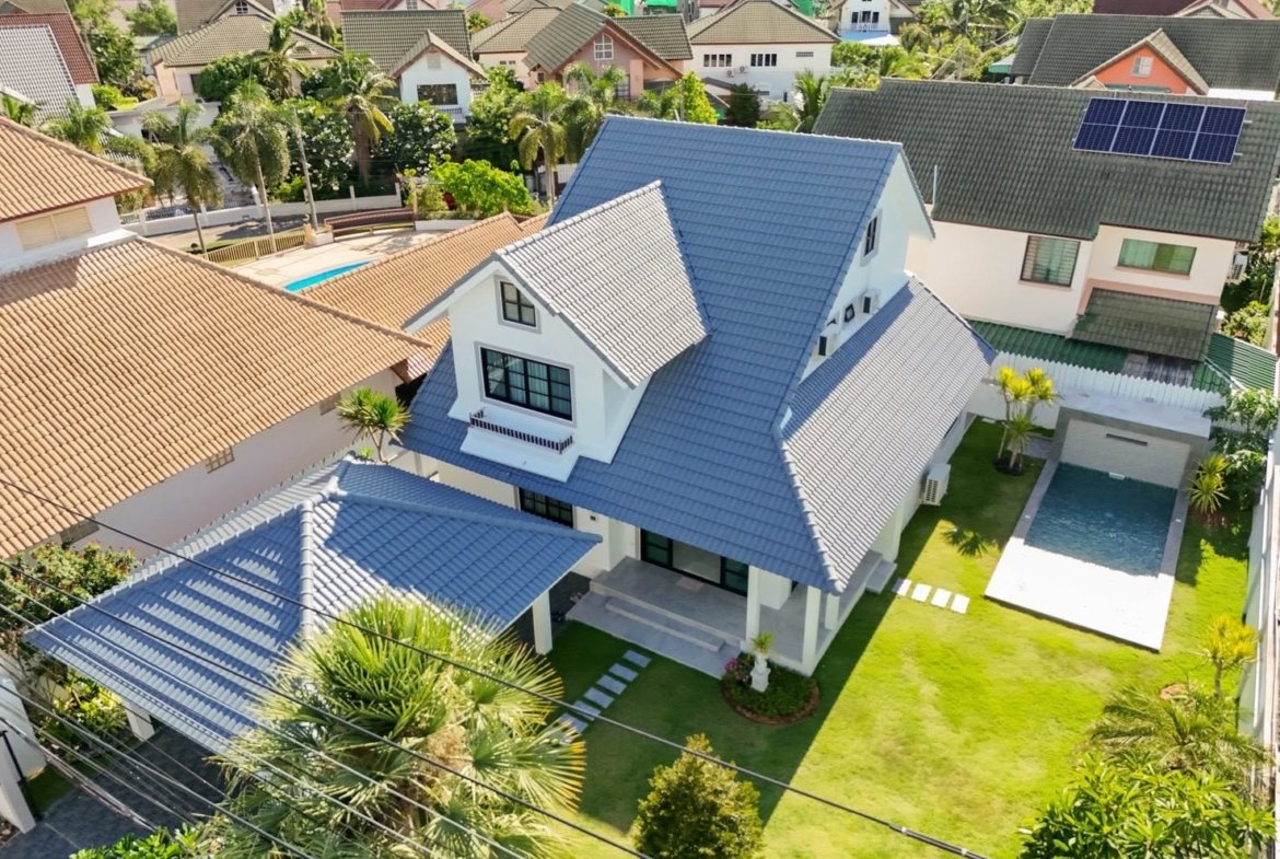 Aerial view of a white two-story house with a blue tile roof and manicured front yard.