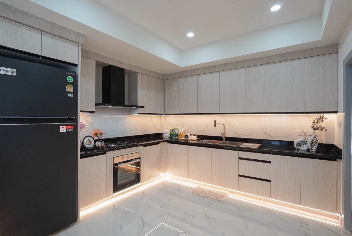 Modern L-shaped kitchen with light gray cabinets, black countertops, built-in oven, and stainless steel sink.