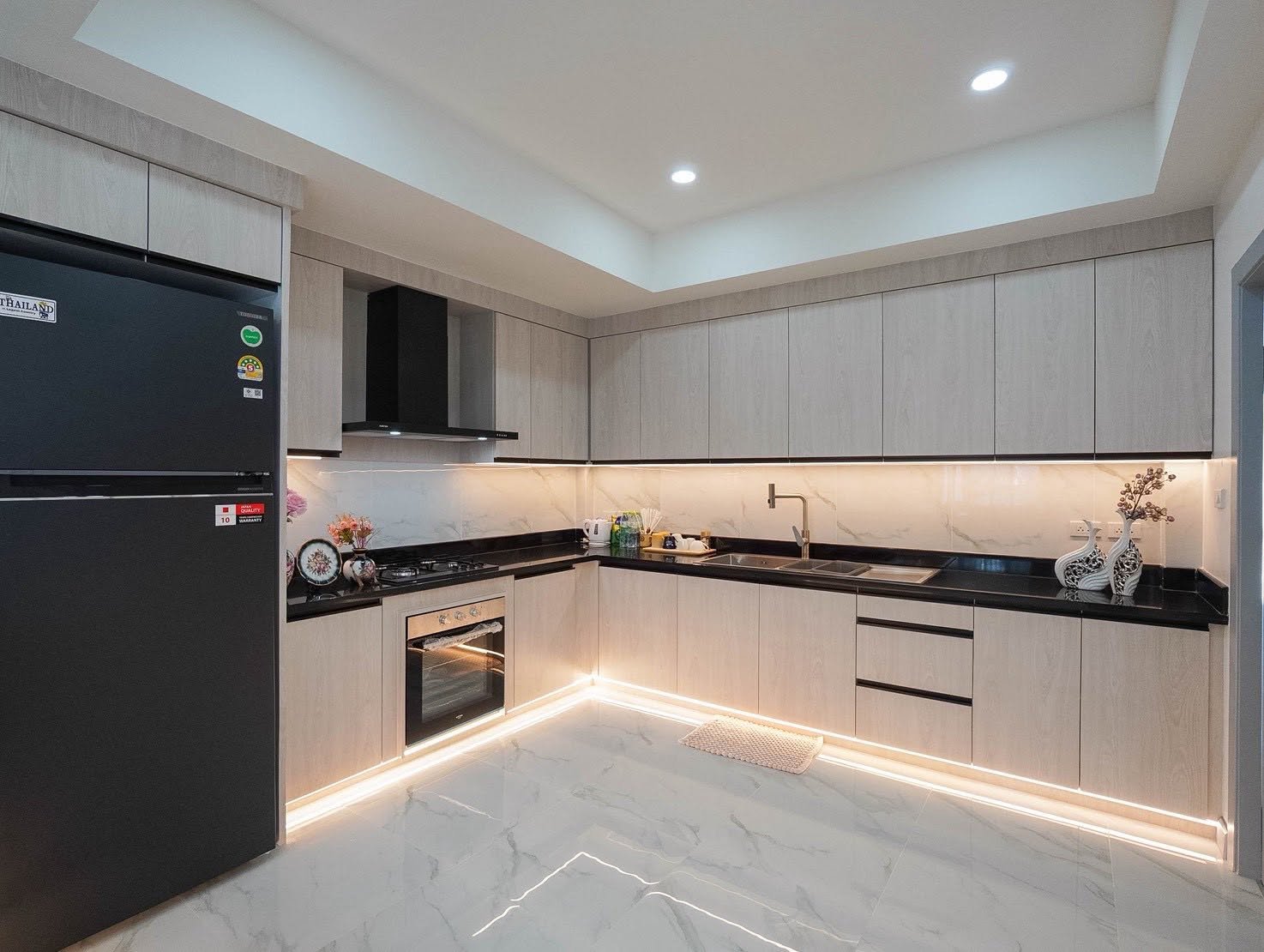 Central_Park_5_Pattaya_Sale_Dlh506_15 Modern L-shaped kitchen with light gray cabinets, black countertops, built-in oven, and stainless steel sink.