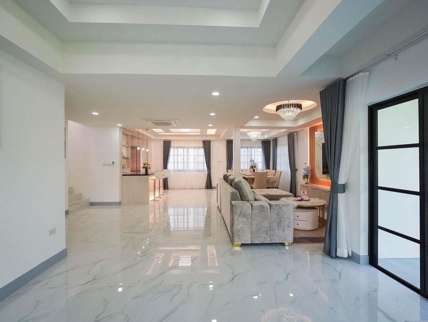 Central_Park_5_Pattaya_Sale_Dlh506_21 Open-plan living room with a marble floor, gray sectional sofa, and a dining area in the background under chandeliers.