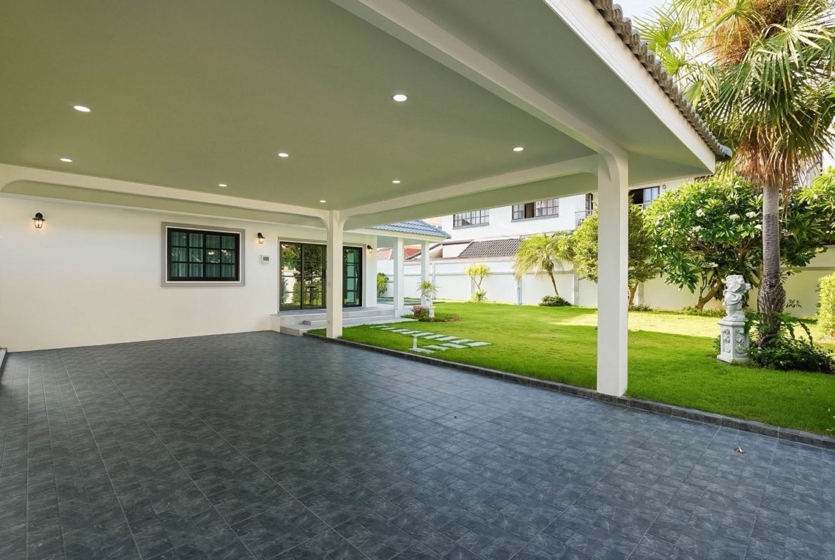 Covered patio with white columns and recessed lights, opening to a green lawn and palm trees.