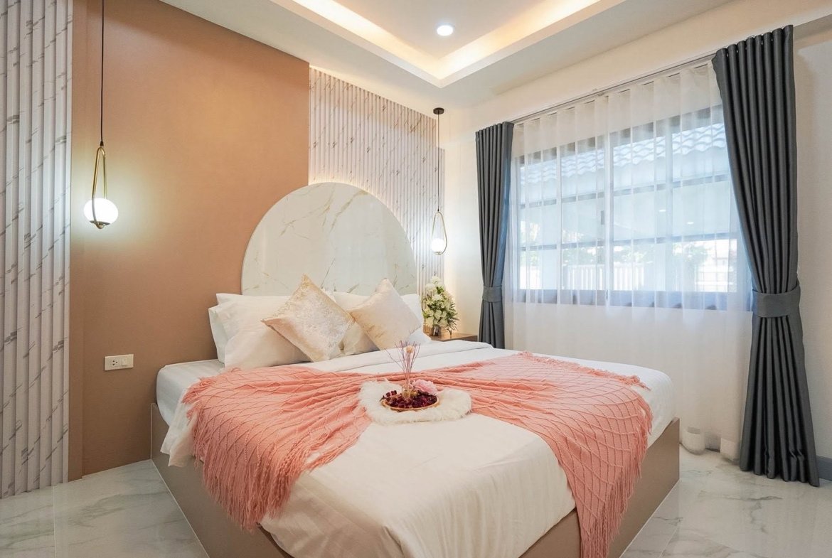 Bedroom with a round marble headboard, pink accent wall, white bedding, and a pink throw blanket.
