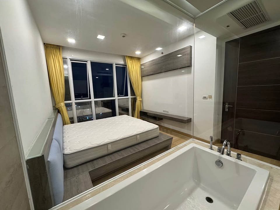 Modern hotel room with a platform bed, white mattress, and a large in-room bathtub in the foreground.
