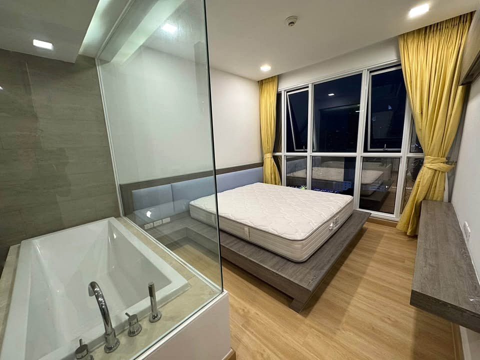 Modern bedroom with a platform bed, glass-walled bathtub, and large night-time window with yellow curtains.