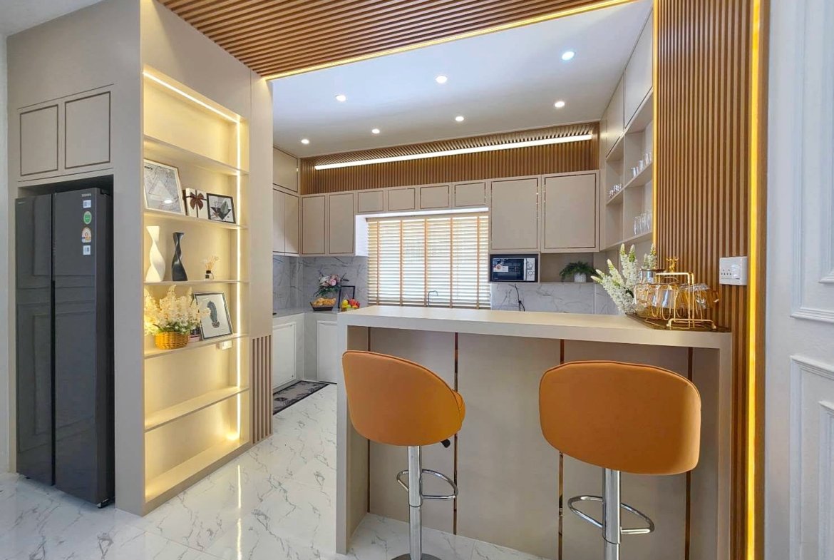 Modern kitchen with an off-white island and two orange bar stools, marble-look floor, and warm wood slat accents.