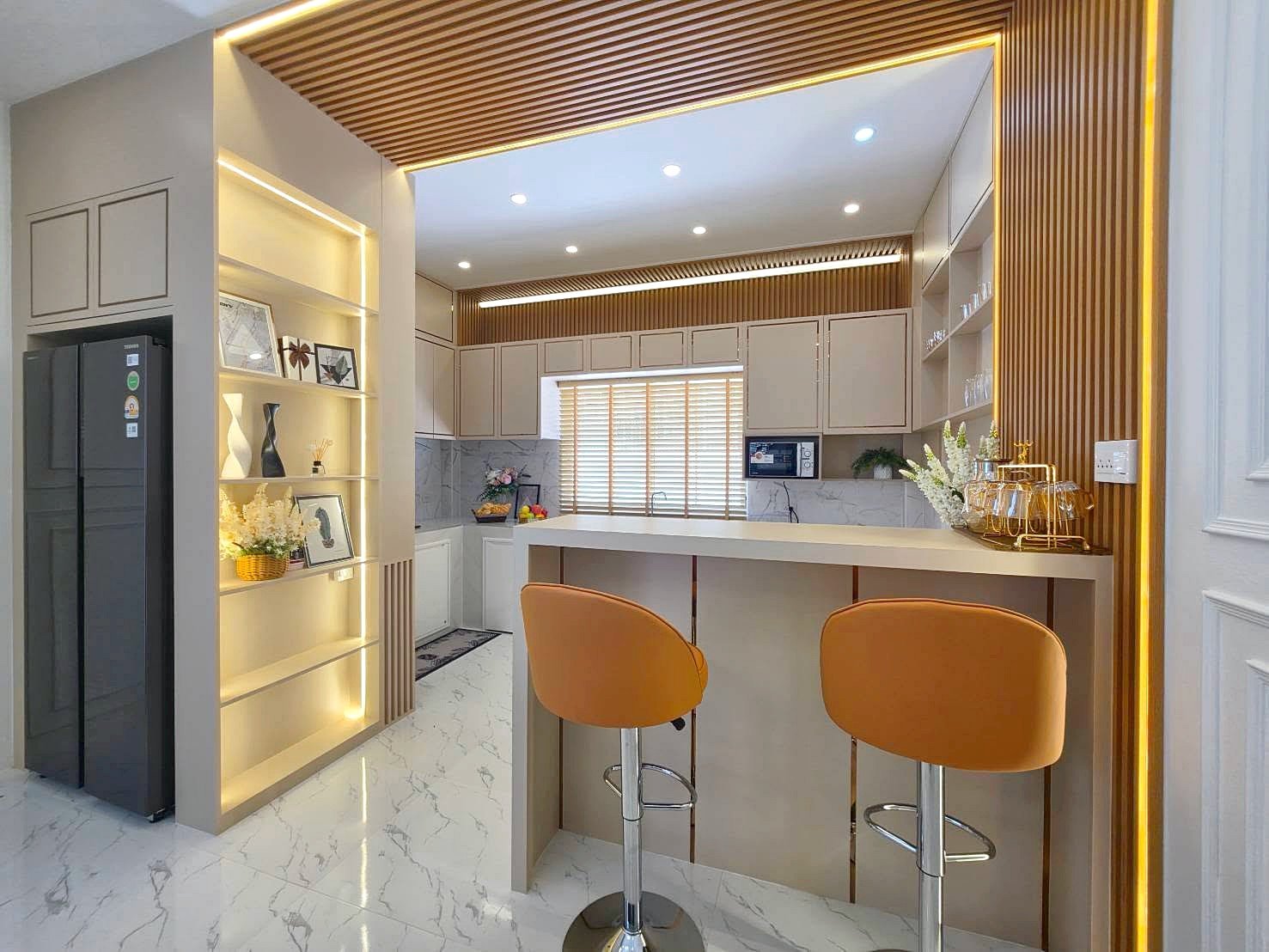 Modern kitchen with an off-white island and two orange bar stools, marble-look floor, and warm wood slat accents.