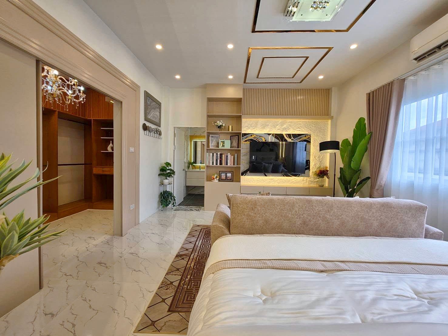 Luxurious bedroom with a beige bed and seating area facing a wall-mounted TV in a softly lit living space.