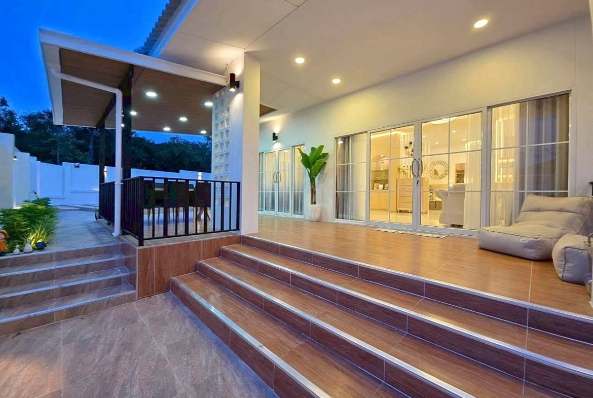 Modern outdoor patio at dusk with wide steps, a covered dining area, and glass doors opening to a bright interiorHidden for accessibility
