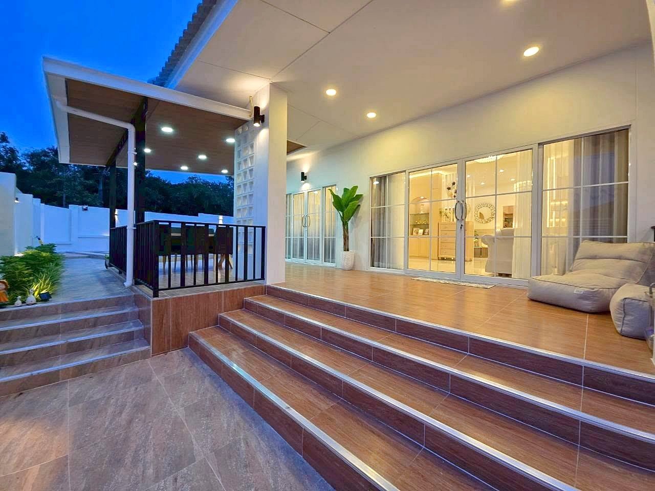 Modern outdoor patio at dusk with wide steps, a covered dining area, and glass doors opening to a bright interiorHidden for accessibility