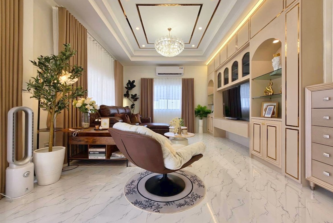 Bright living room with marble floor, beige curtains, brown sofa, swivel chair, and a built-in entertainment wall with a chandelier overhead.