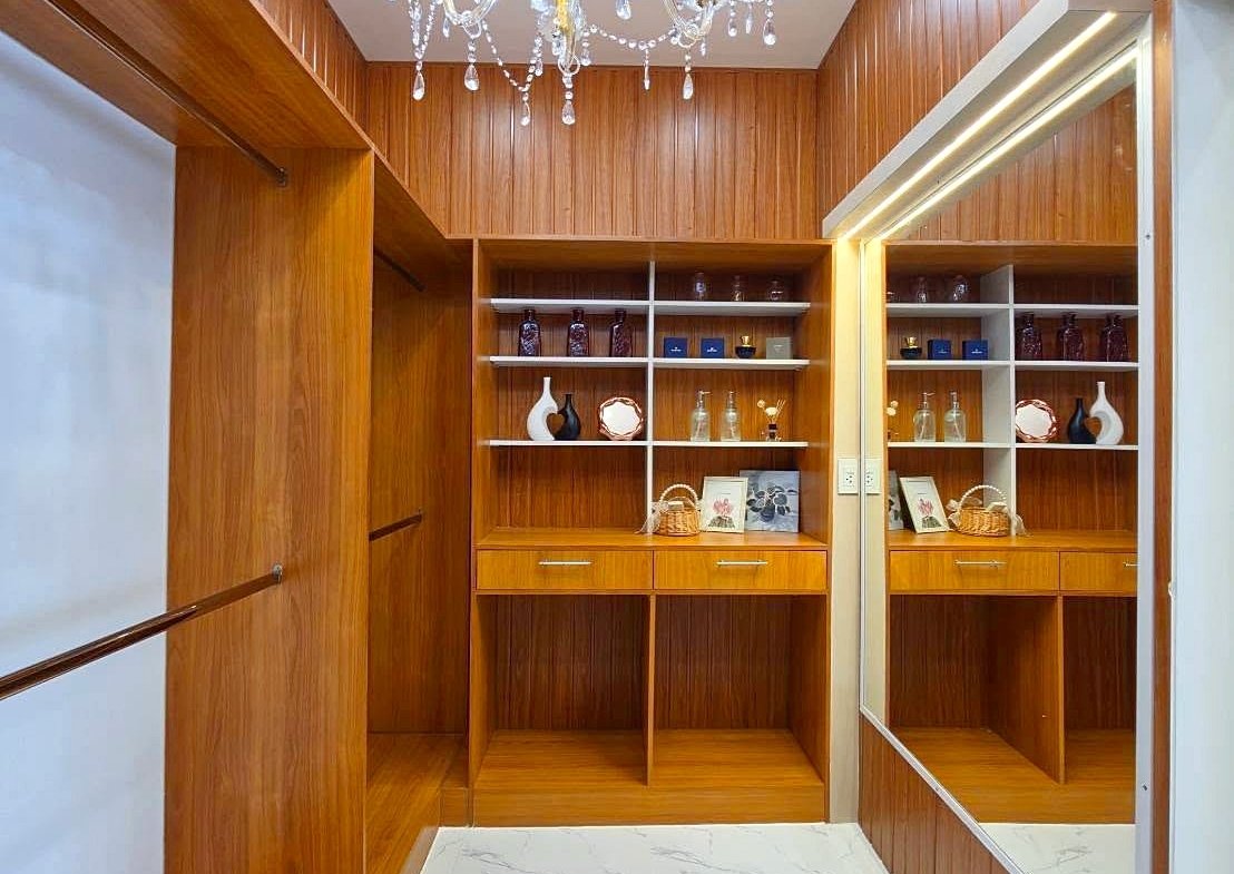 Bright wooden walk-in closet with built-in shelves, drawers, and a crystal chandelier overhead.