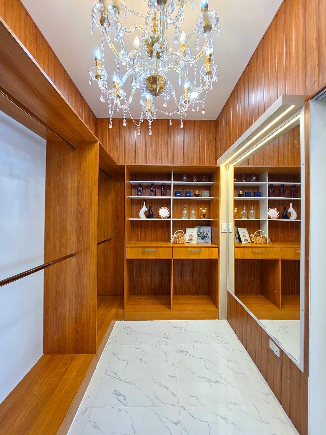 Bright wooden walk-in closet with built-in shelves, drawers, and a crystal chandelier overhead.