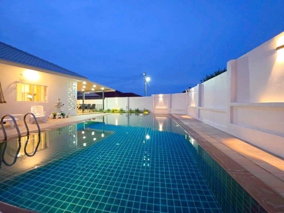 Evening view of a rectangular backyard pool with blue tiled water white walls and warm patio lights