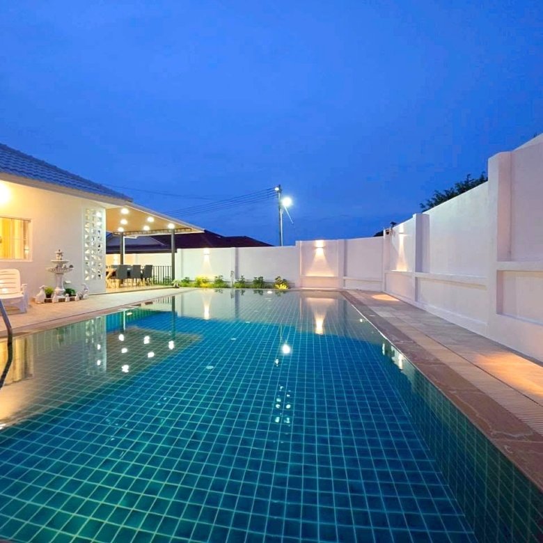 Evening view of a rectangular backyard pool with blue tiled water white walls and warm patio lights