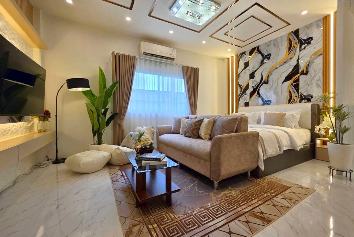 Luxurious hotel suite living area with beige sofa, bed, and marble-tiled floor under geometric ceiling design.