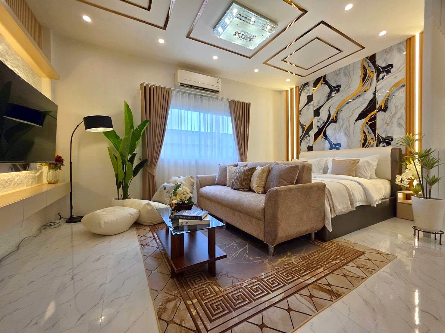 Luxurious hotel suite living area with beige sofa, bed, and marble-tiled floor under geometric ceiling design.