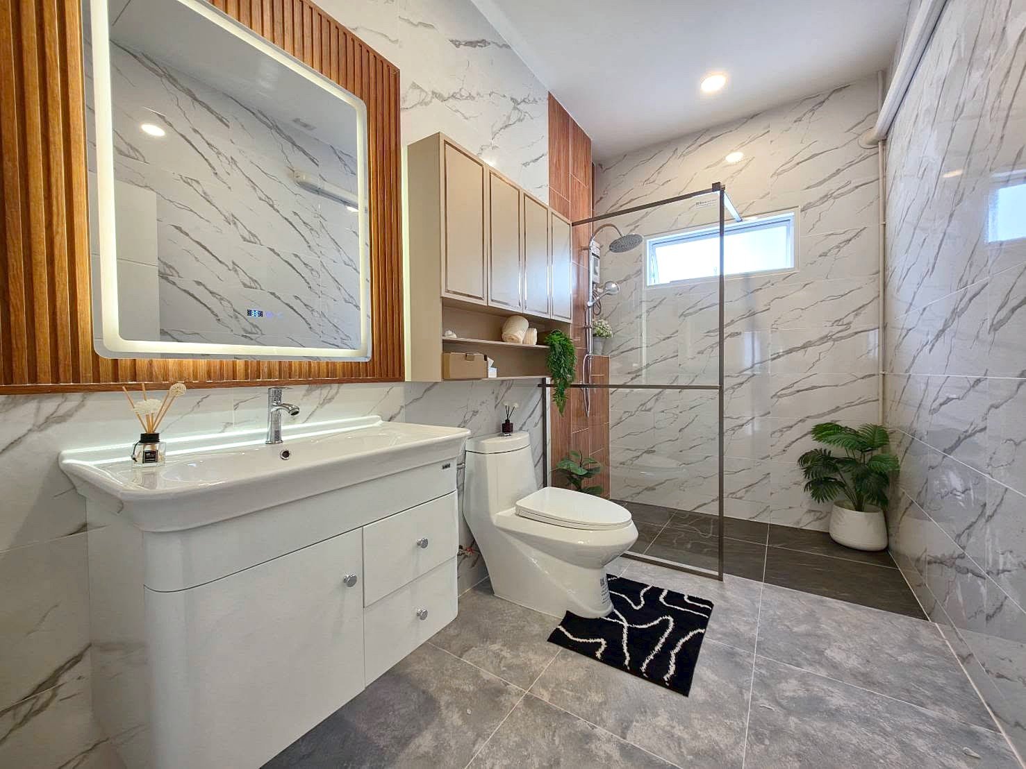 Modern bathroom with marble walls, white vanity, toilet, and glass-enclosed shower; potted plants add greenery.