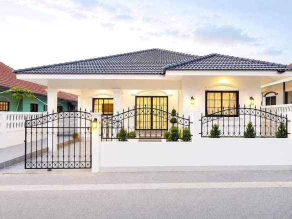 White single story house with black wrought iron gate and decorative fence illuminated entrance and windows potted plants along the front