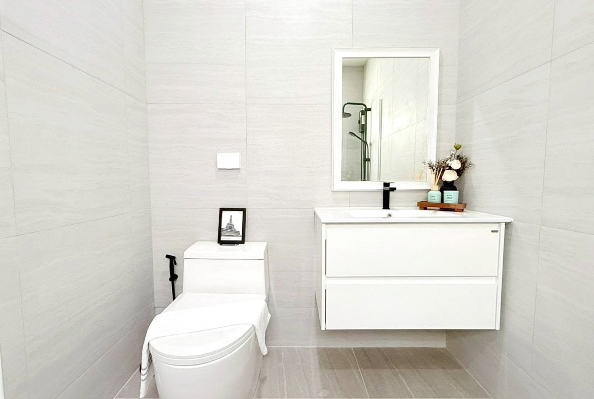Modern white bathroom with a wall-mounted vanity, large mirror, and toilet; decorative toiletries on the counter.