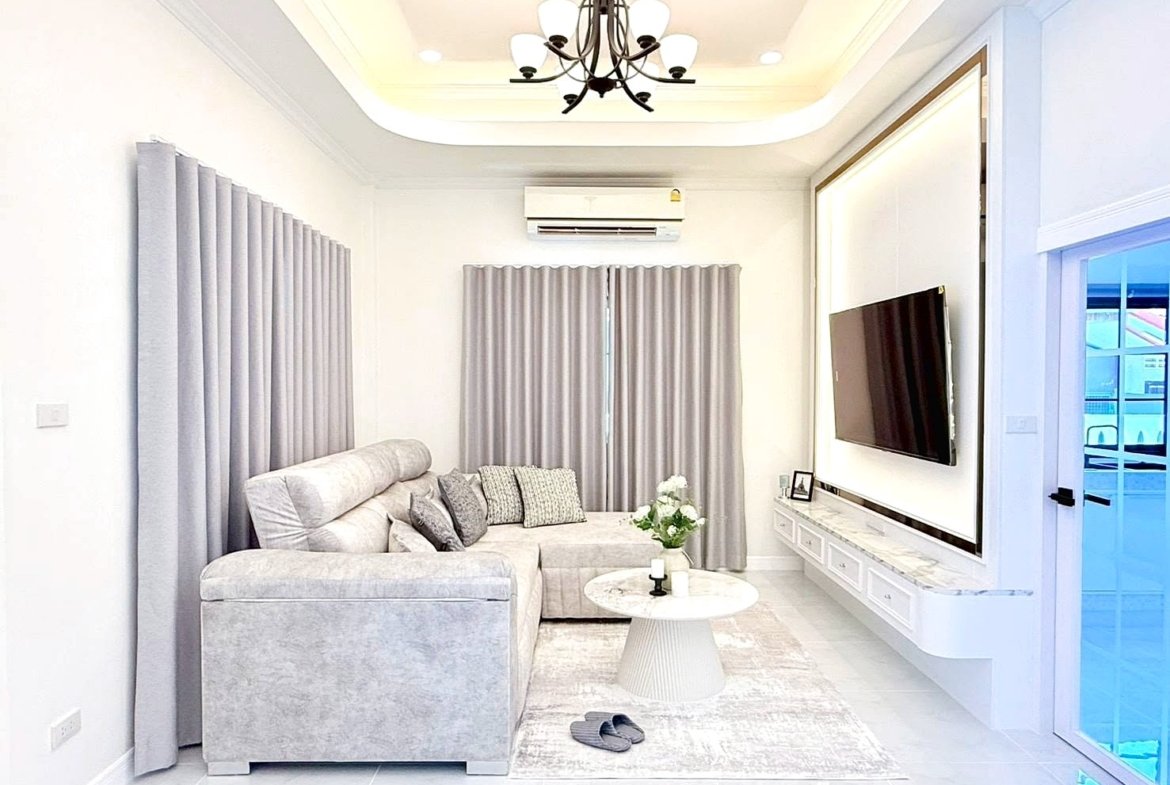 Bright, contemporary living room with a light gray sectional sofa, gray curtains, and a wall-mounted TV on a marble-topped console.
