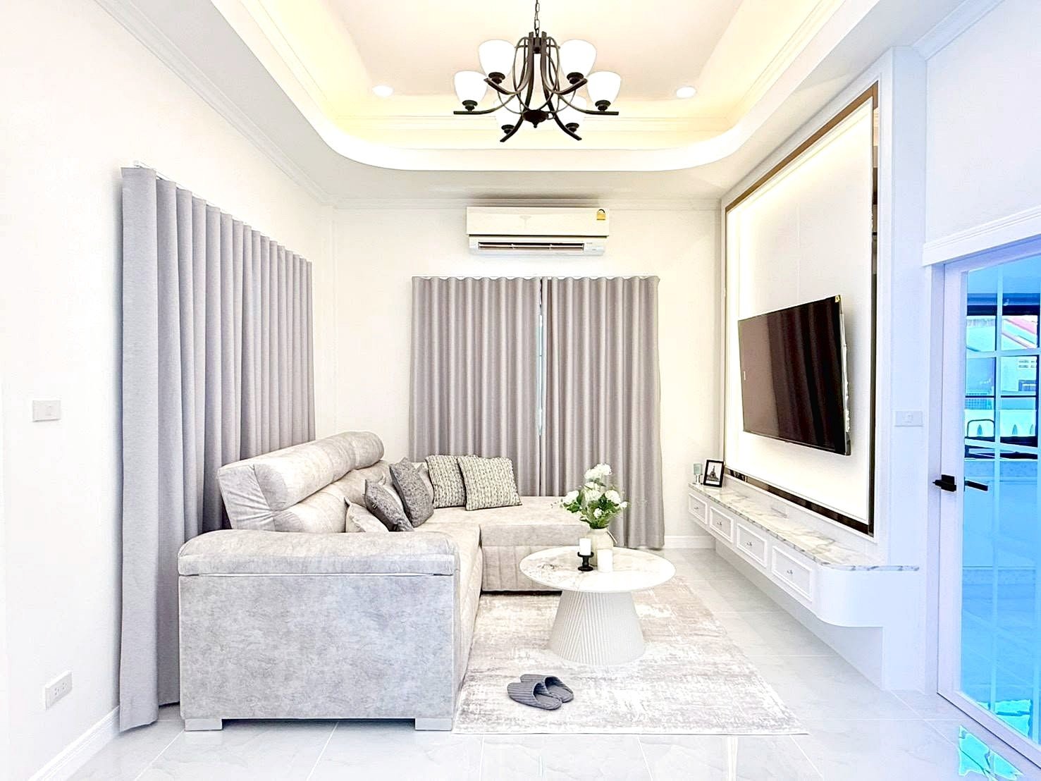 Bright, contemporary living room with a light gray sectional sofa, gray curtains, and a wall-mounted TV on a marble-topped console.