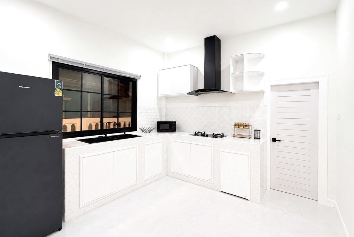 Bright, modern white kitchen with a black side-by-side fridge, gas stove, range hood, and white cabinets along two walls