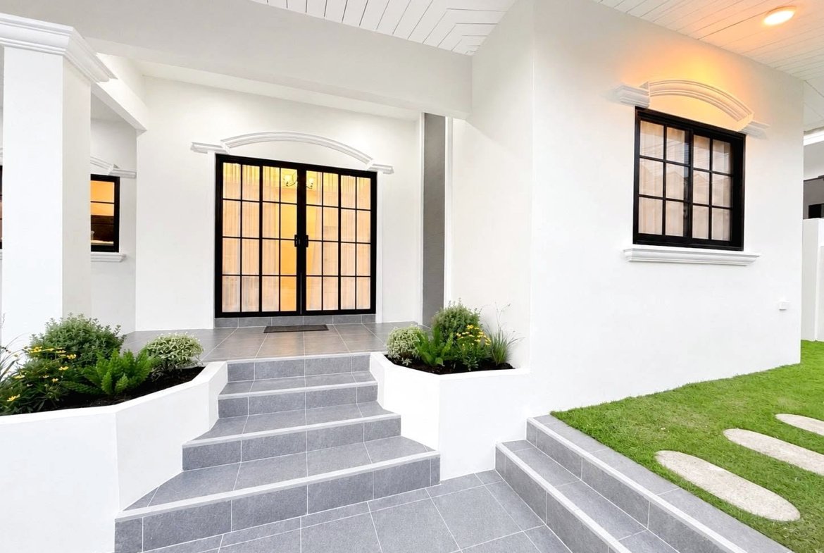 White modern house entry with gray tile steps and black-framed glass doors, surrounded by small garden beds.
