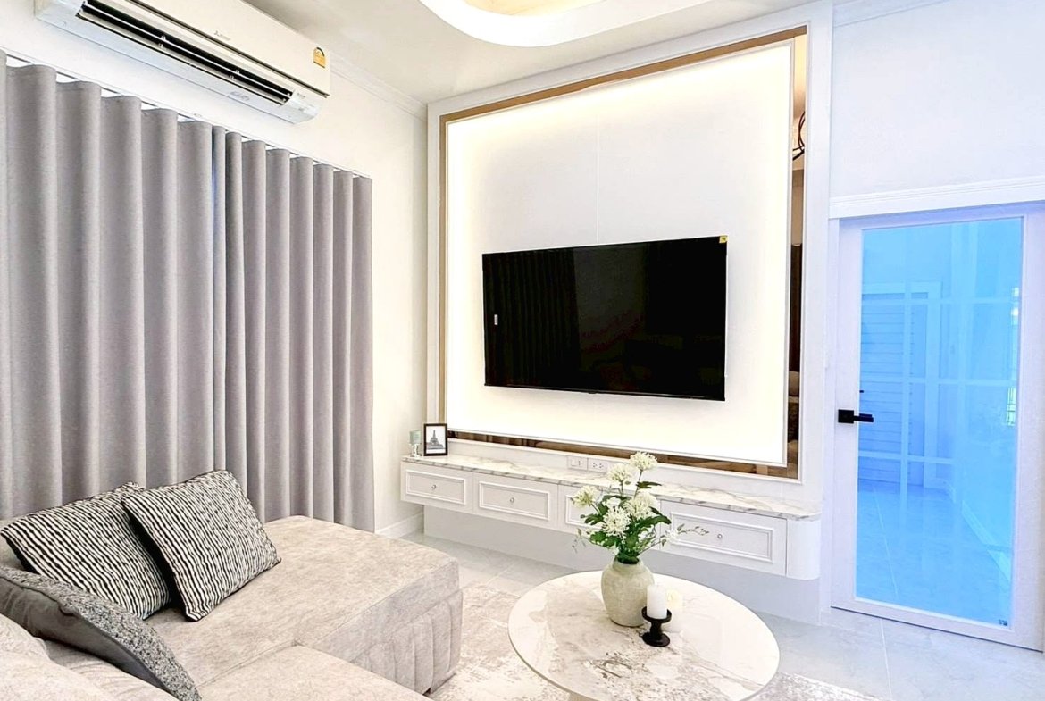 Modern living room with a wall-mounted flat-screen TV on a backlit frame, white marble console, and gray sofa with striped cushions.