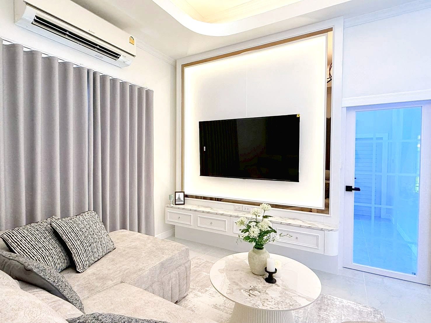 Modern living room with a wall-mounted flat-screen TV on a backlit frame, white marble console, and gray sofa with striped cushions.