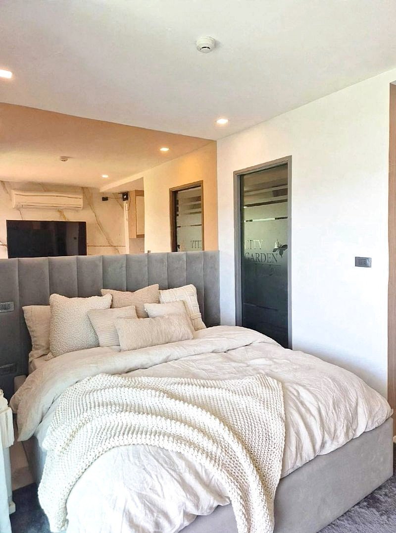 Cozy modern bedroom with a tall gray upholstered bed, white bedding, and multiple cream pillows.