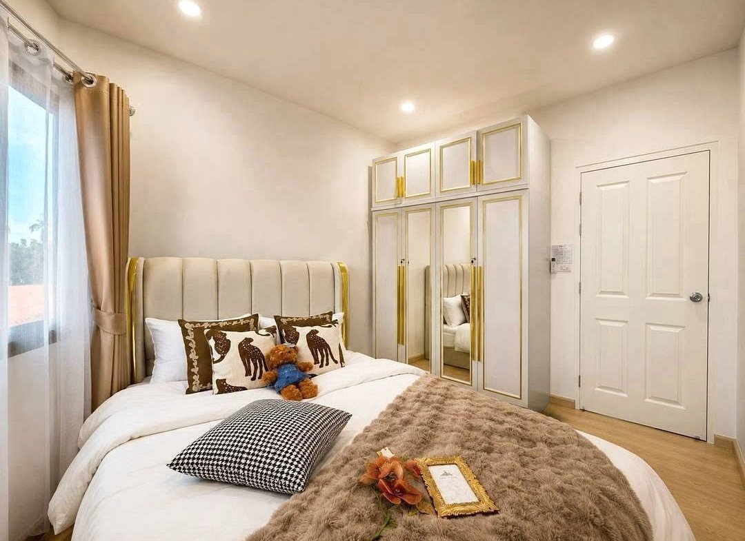 Bright modern bedroom with a cream tufted headboard, gold-trimmed wardrobes, and a white bed with a plush fur throw.
