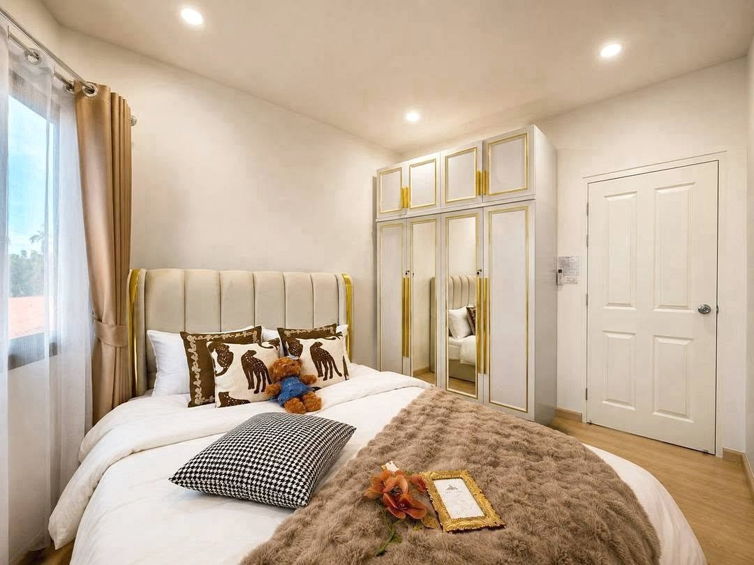 Deperfect_Village_a1_Rdl365_11 Bright modern bedroom with a cream tufted headboard, gold-trimmed wardrobes, and a white bed with a plush fur throw.